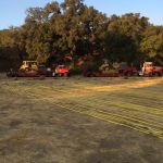 Bull dozers loaded on tractor trailers with fire hoses in the foreground