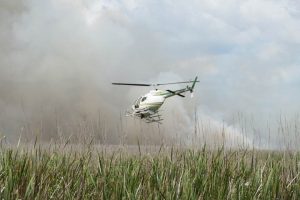 Helicopter used to fight wildfire flying low over a marsh