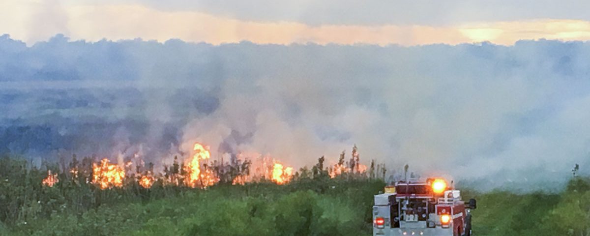 Fire truck next to a fire buring in an open area