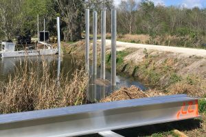 Levee cutting across a wetland with metal beams jutting out of the water