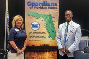 Two procurement staff members standing with district banner stand