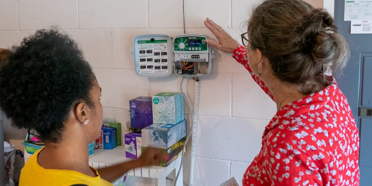 eirdre Irwin shows Miky Ynirio how to adjust her lawn sprinkler timer
