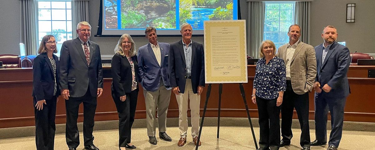 Board members and Dr, Shortelle standing around a tripod holding a proclamation