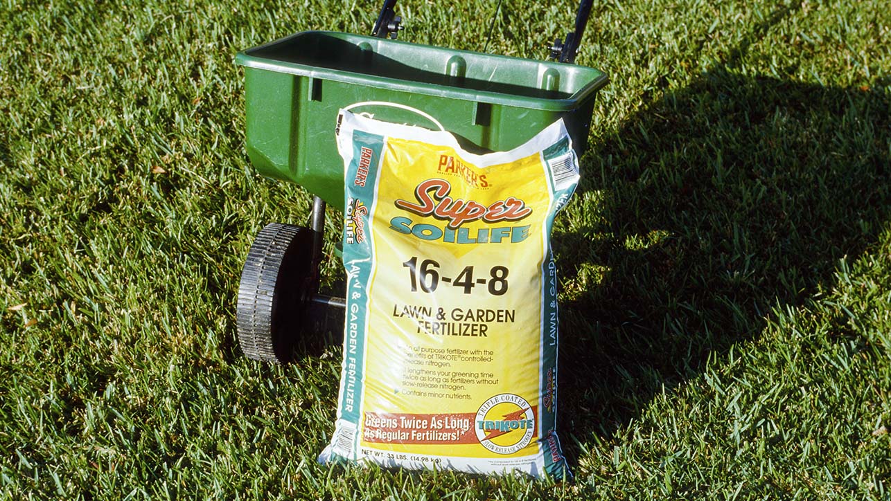 A bag of fertilizer leaning against a fertilizer spreader