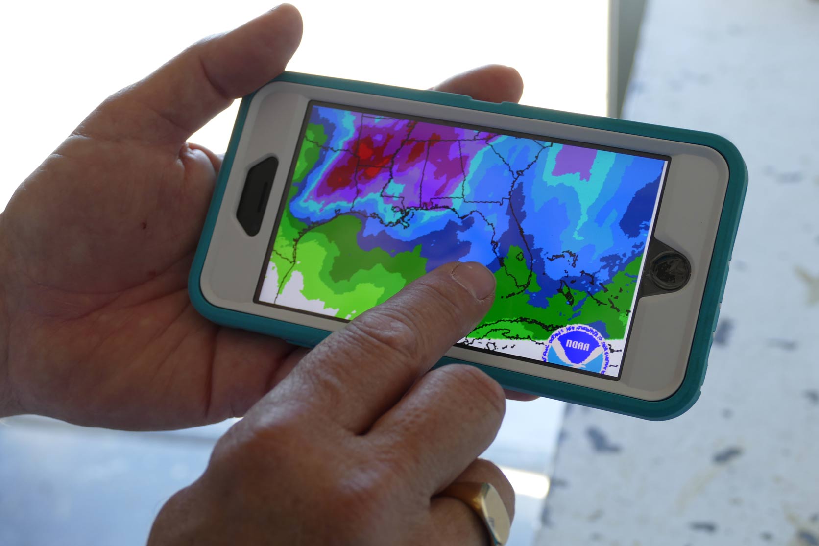 Person tapping a cell phone showing weather
