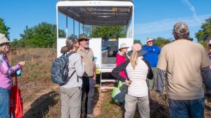 a group of people standing behind a white semi enclosed trailer in a field
