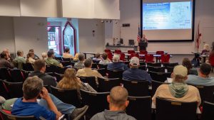 environmental scientist, Josh Papacek, speaking at a podium in front of a room full of people