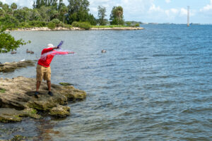 a fisherman in a red shirt casting a net into the water