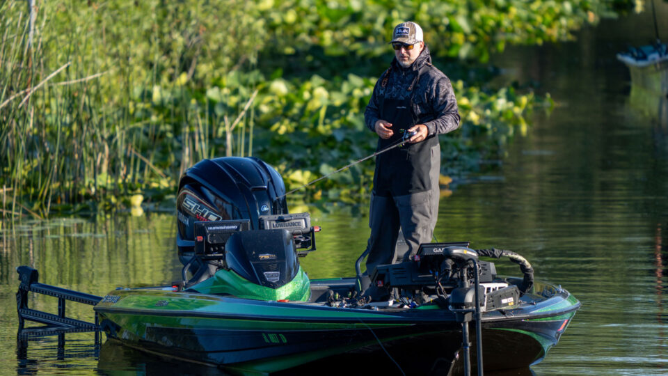 Man standing in boat fishing near shoreline vegetation