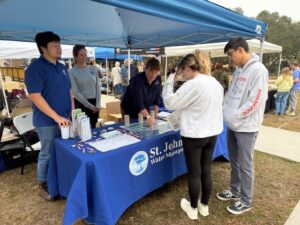 St. Johns River Water Management District staff and volunteers engage with community members at an informational booth under a blue tent, with visitors examining educational materials on a branded table