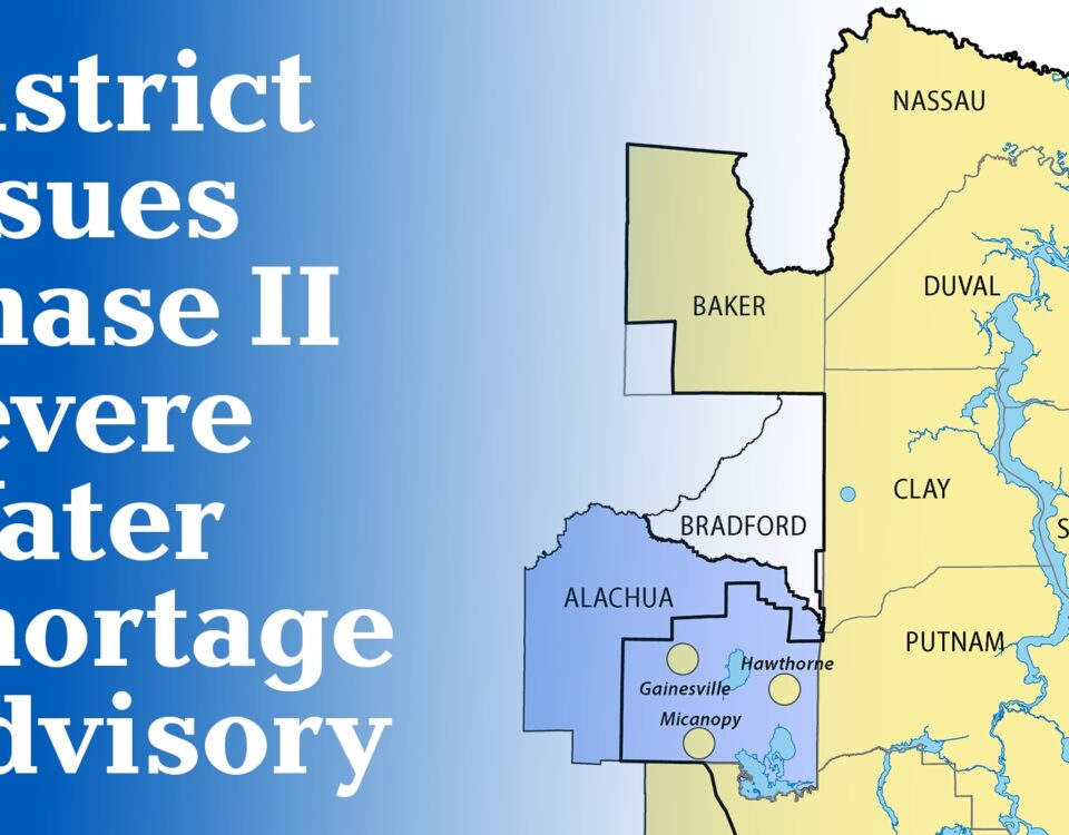 A map graphic announcing a Phase II Severe Water Shortage Advisory issued by the water management district, showing the affected area highlighted in blue covering Alachua and Bradford counties, with cities Gainesville, Micanopy, and Hawthorne marked, surrounded by the yellow-shaded counties of Nassau, Baker, Duval, Clay, St. Johns, Putnam, and Flagler within the district boundary