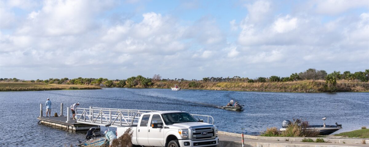 white truck backing a boat trailer into the water on a concrete boat ramp