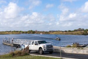 white truck backing a boat trailer into the water on a concrete boat ramp