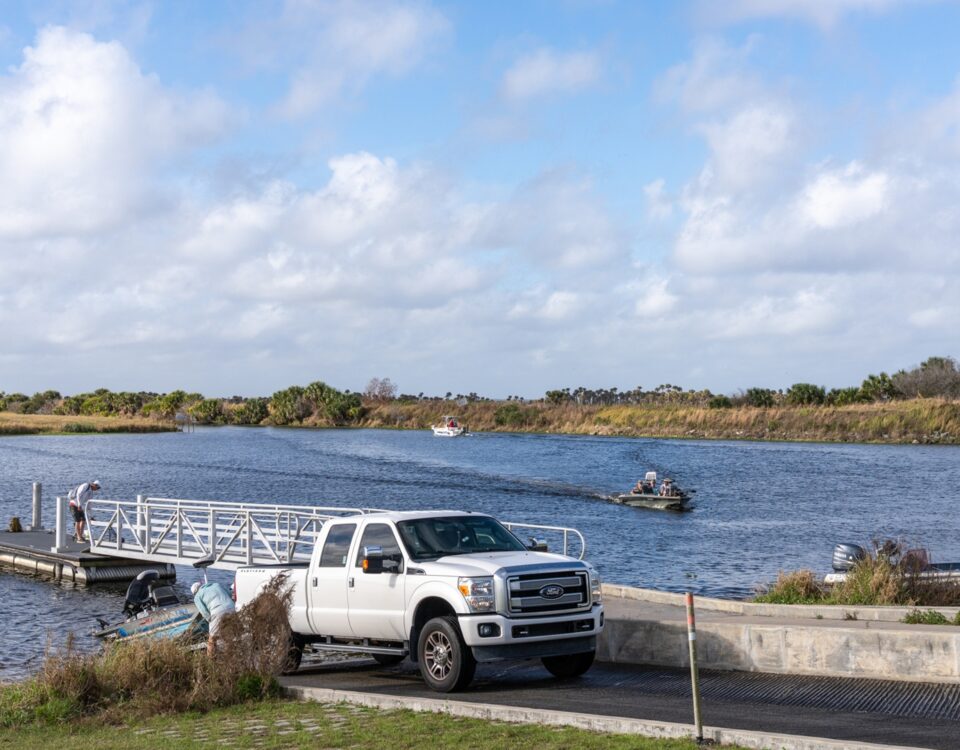 white truck backing a boat trailer into the water on a concrete boat ramp