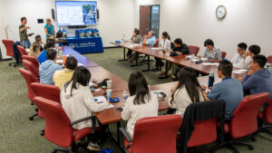 A group of Taiwan delegates and district staff sit around a U‑shaped conference table listening to a water quality monitoring presentation, with a large screen at the front displaying maps and photos and a St. Johns River Water Management District table draped in blue in the background.