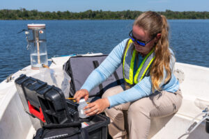 Water management district field staff collects a water sample from a boat using monitoring equipment on a lake.