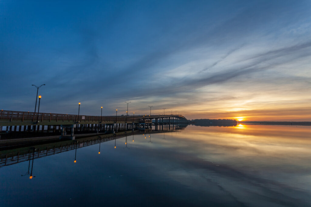 Sunrise over the St. Johns River in Palatka, with a bridge extending across calm water and reflections of lights on the river.