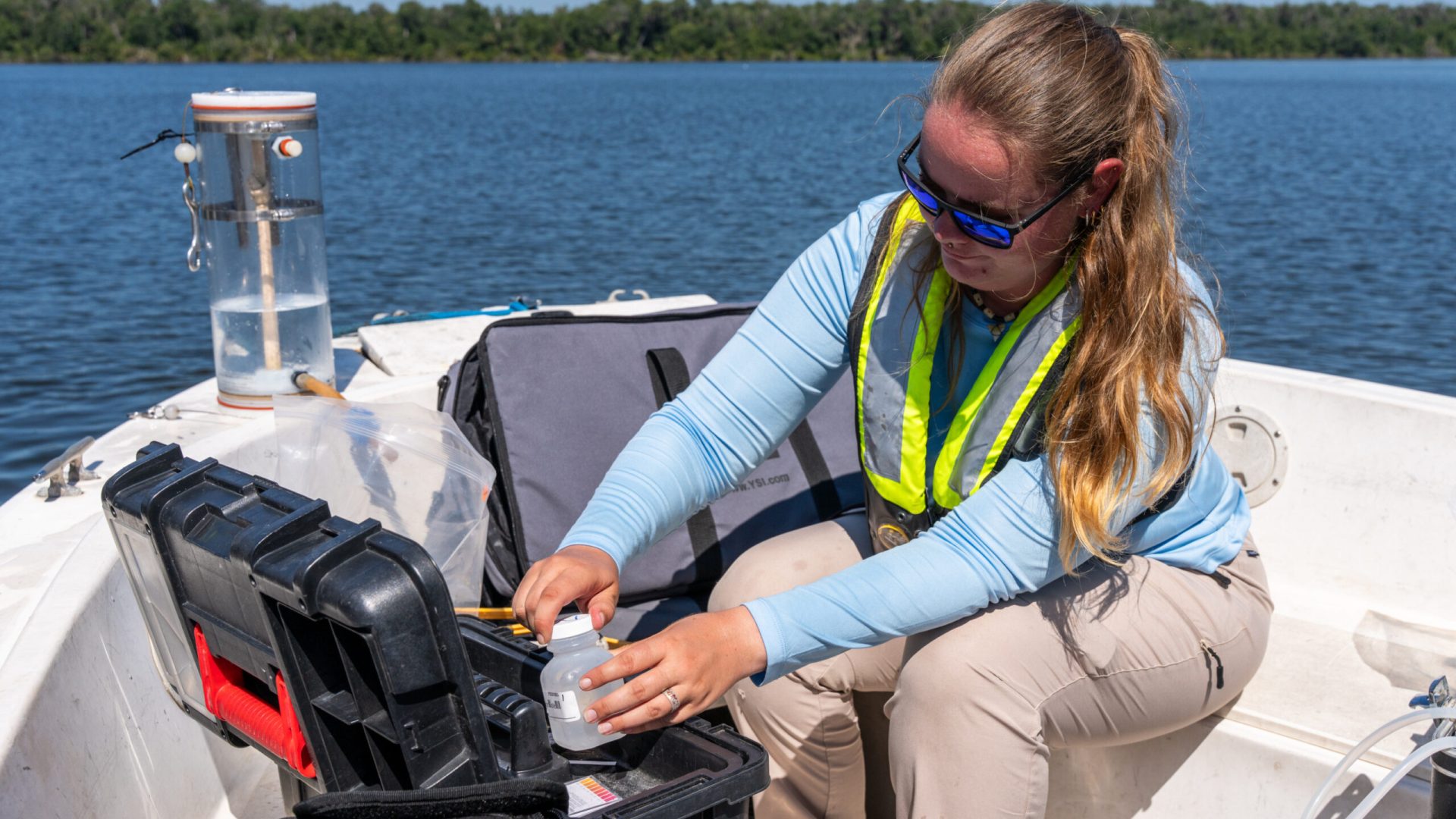 Water management district field staff collects a water sample from a boat using monitoring equipment on a lake.