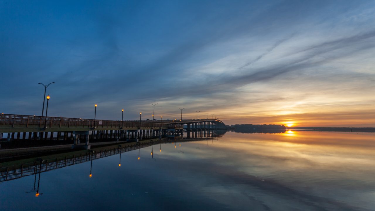 Sunrise over the St. Johns River in Palatka, with a bridge extending across calm water and reflections of lights on the river.